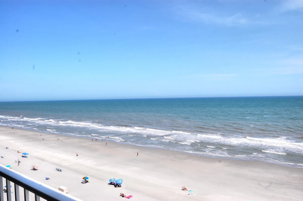 This image captures a lively beachfront scene with ocean waves, sandy shores, people sunbathing, swimming, and colorful beach umbrellas scattered along the sand. The atmosphere is both tranquil and joyful, highlighting classic beach activities and the vibrant energy of Myrtle Beach.