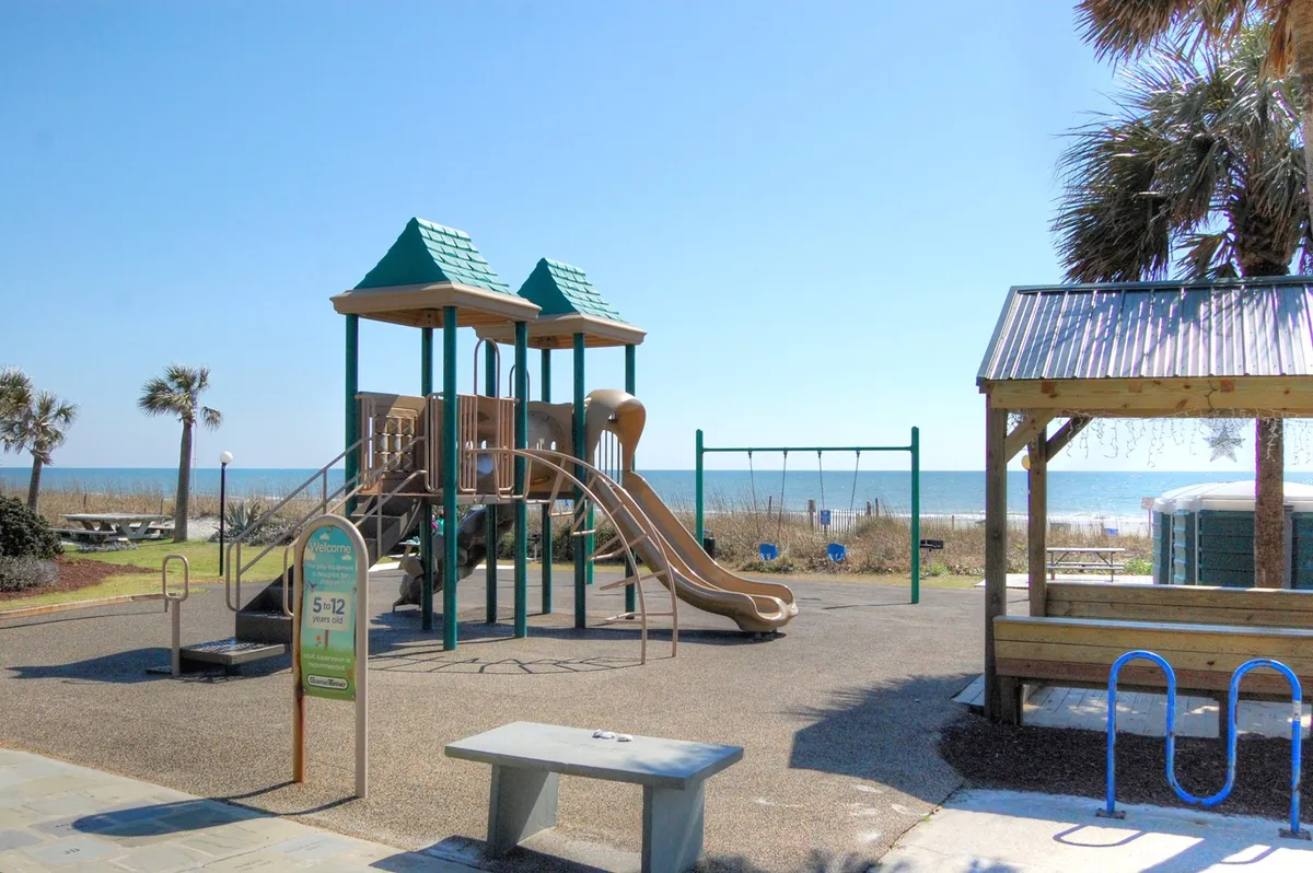 A colorful playground set with swings and palm trees, all set against an ocean view backdrop. The space is lively and family-friendly, encouraging outdoor activity for all ages.