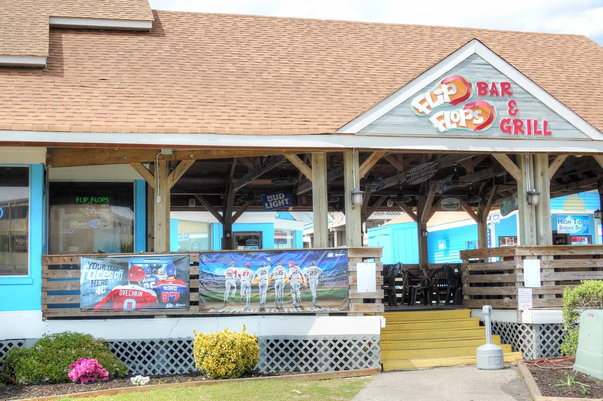 A lively exterior of a local restaurant sign 'Flip Flops Bar & Grill' with colorful banners and an inviting outdoor seating area. The festive atmosphere captures the spirit of Myrtle Beach’s dining scene.