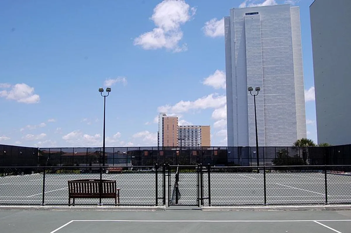 Well-maintained outdoor tennis courts with benches and surrounding buildings in view. The area is lively, ready for friendly matches or casual hangouts, reflecting the energetic spirit of resort activities.