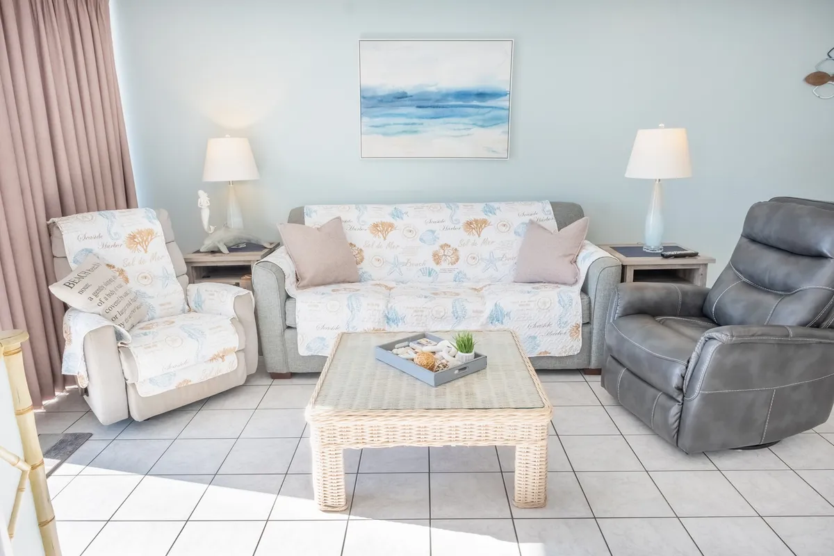 A welcoming living area with a sea-themed sofa, recliner chair, and a coffee table adorned with decor. Framed artwork on the wall and soft lighting create a calm, comfortable atmosphere ideal for morning coffee, reading, or gathering with friends and family.