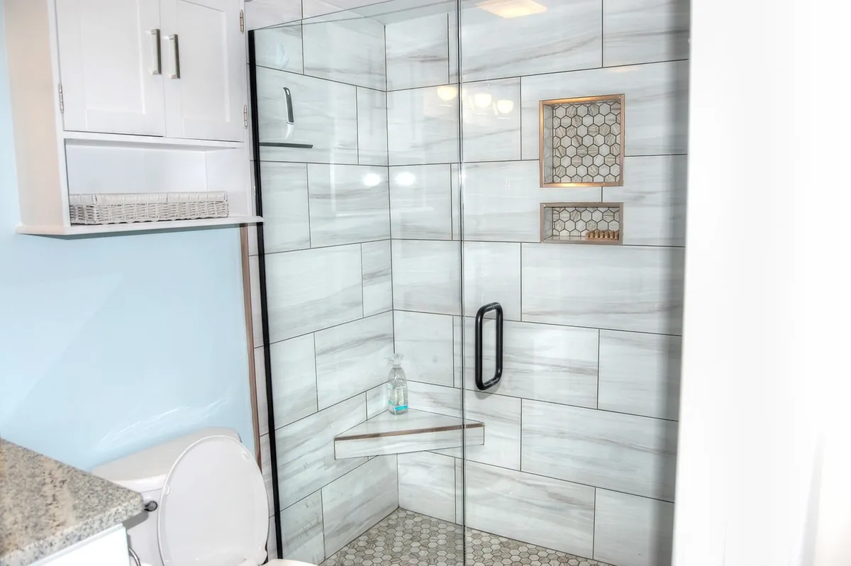 A modern bathroom featuring a glass shower enclosure, hexagonal tile floor, and a built-in shelf. The ambiance is calm and rejuvenating, inviting guests to unwind after the day's adventures.